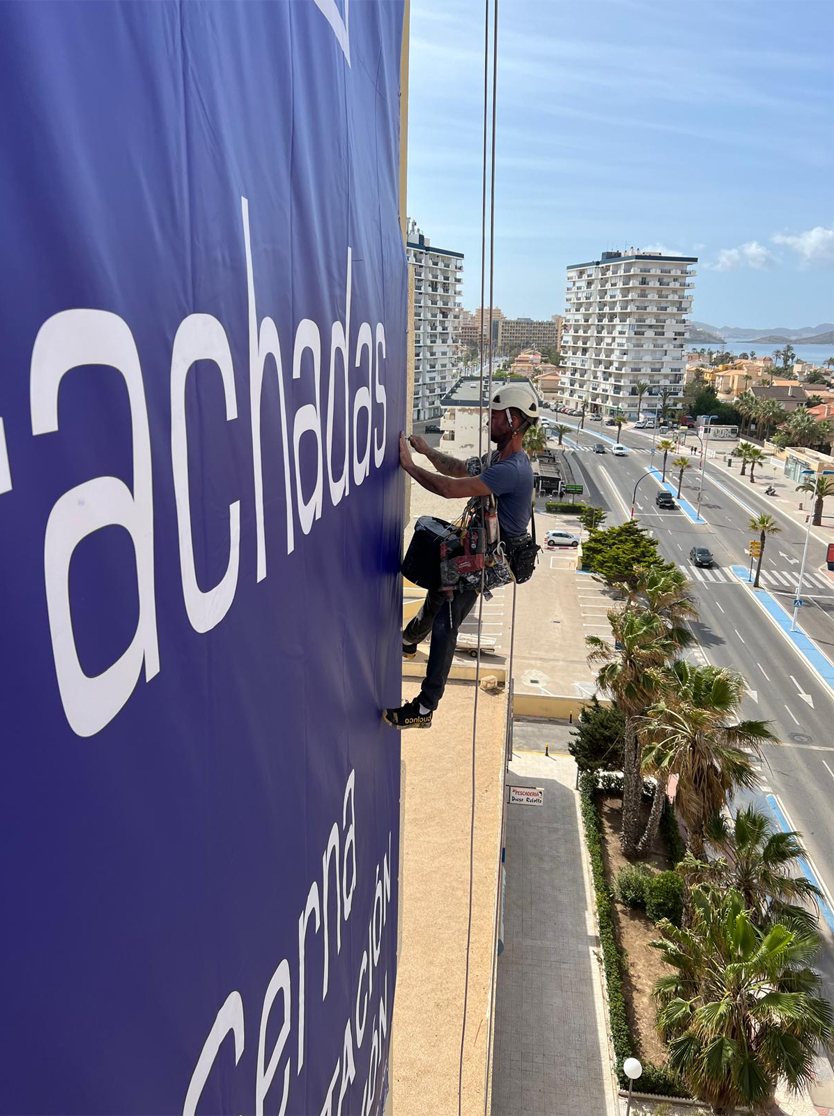 Trabajador especializado en trabajos verticales en Murcia instalando una lona en altura con equipos de seguridad avanzada.